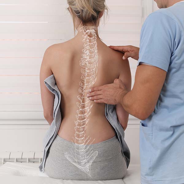 Mujer sentada de espaldas con un doctor que le toca la columan vertebral representada por encima de la foto con un dibujo